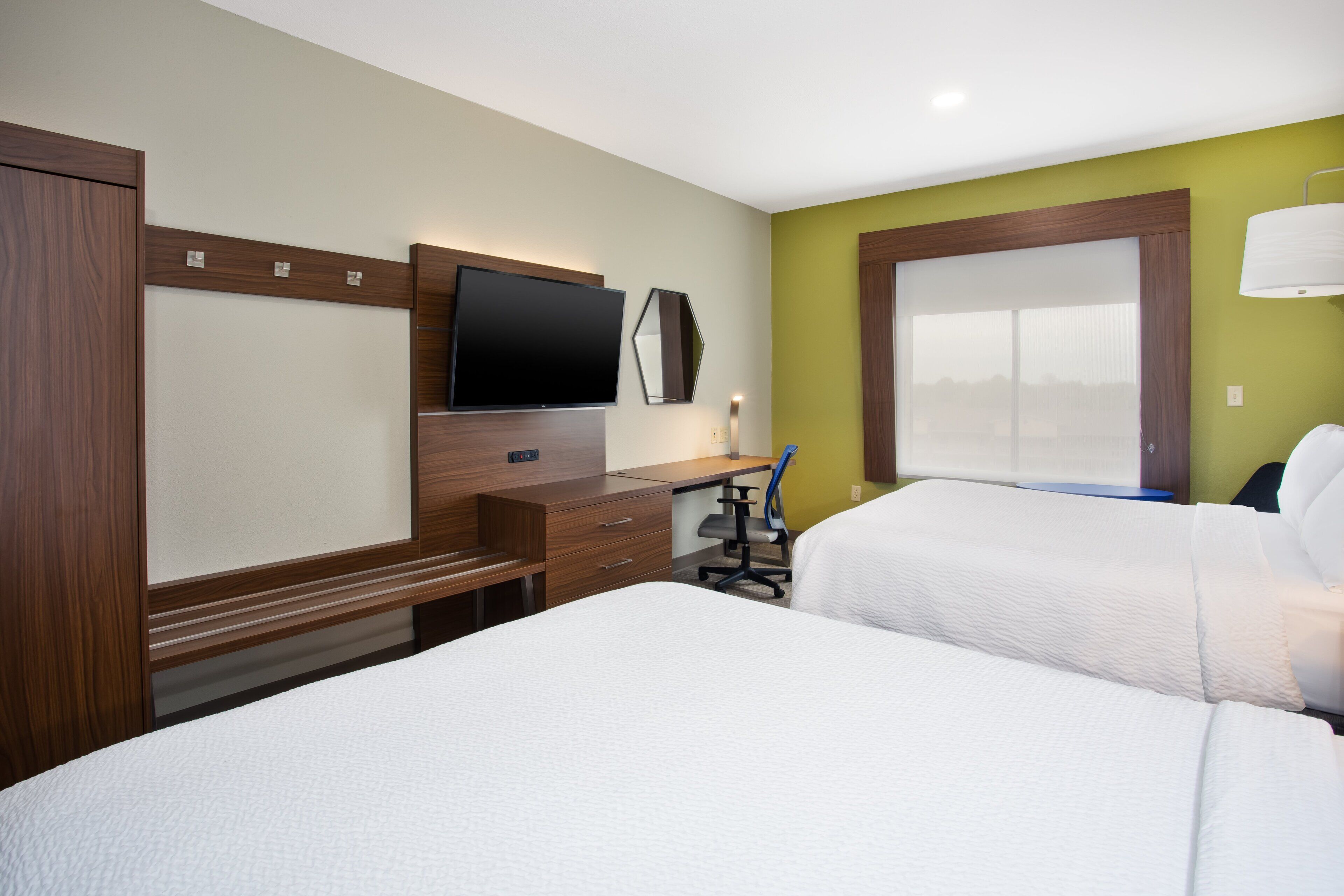 A hotel room with two beds, a desk, a flat-screen TV, and a window.