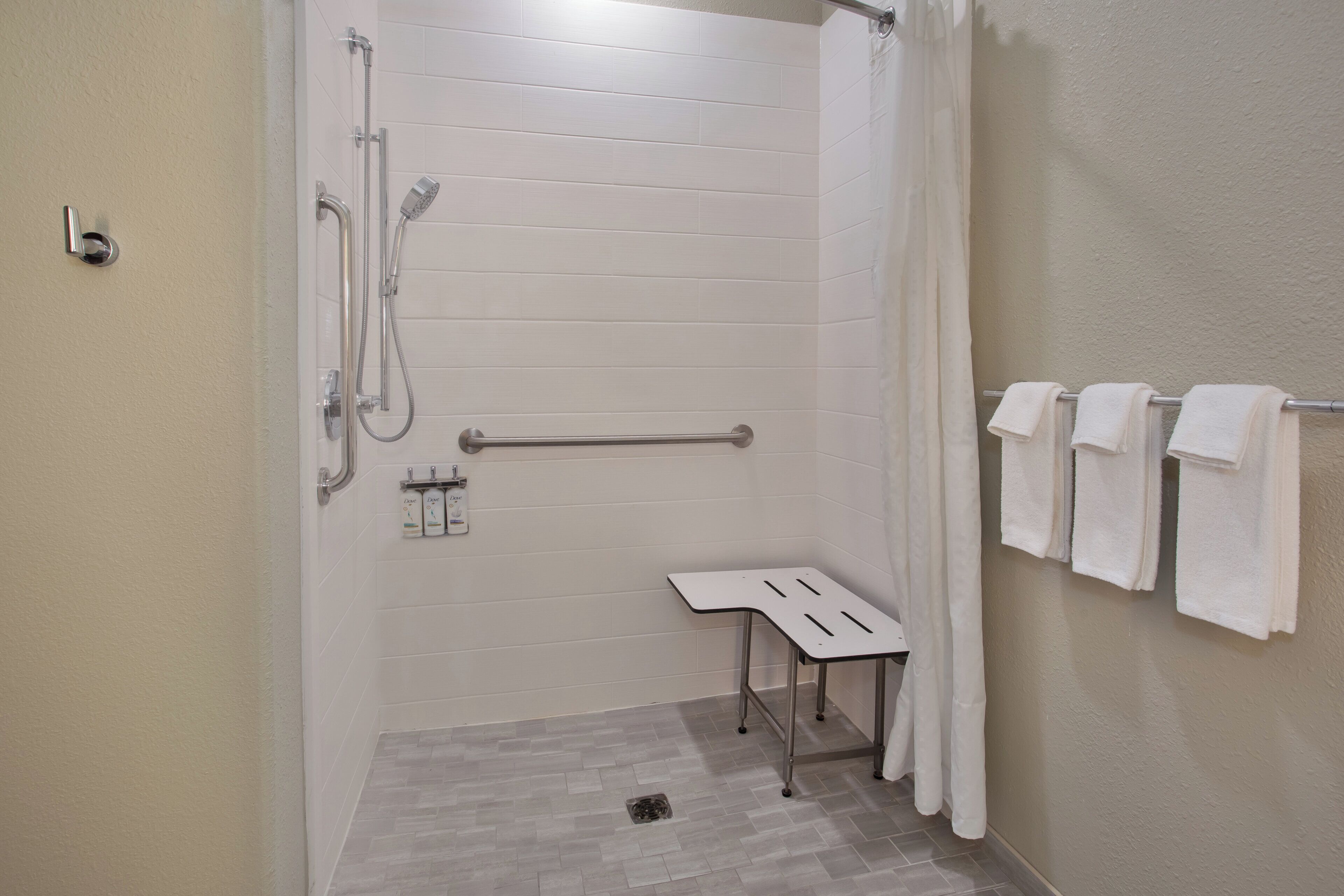 Un baño con ducha, barras de apoyo, toallero y una mesita.