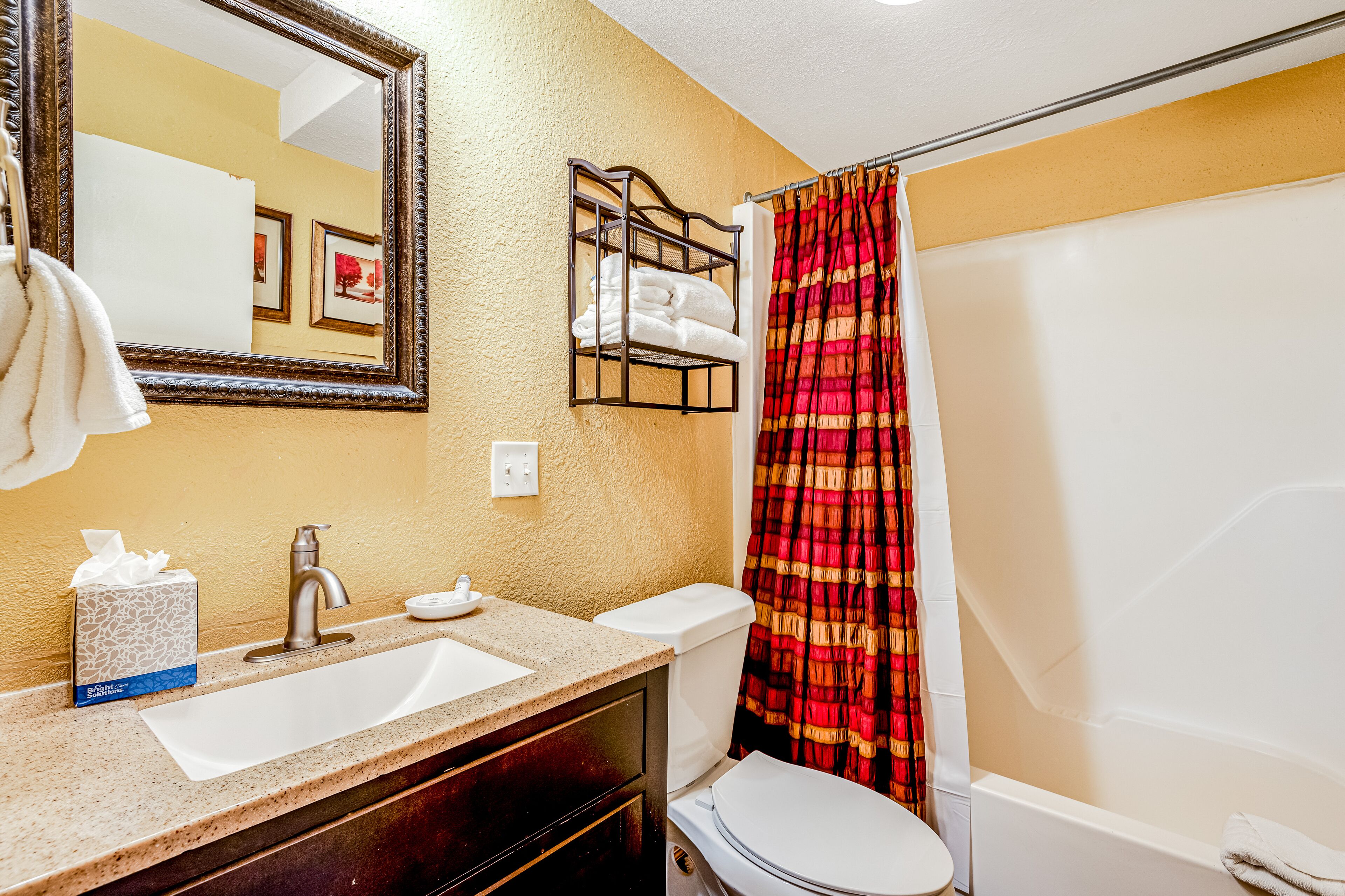 Une salle de bain équipée d’un lavabo, d’un miroir, de toilettes et d’un rideau de douche.