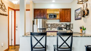 Cocina moderna con armarios de madera, refrigerador de acero inoxidable, microondas y encimera de granito. Hay dos sillas negras de diseño al panel.