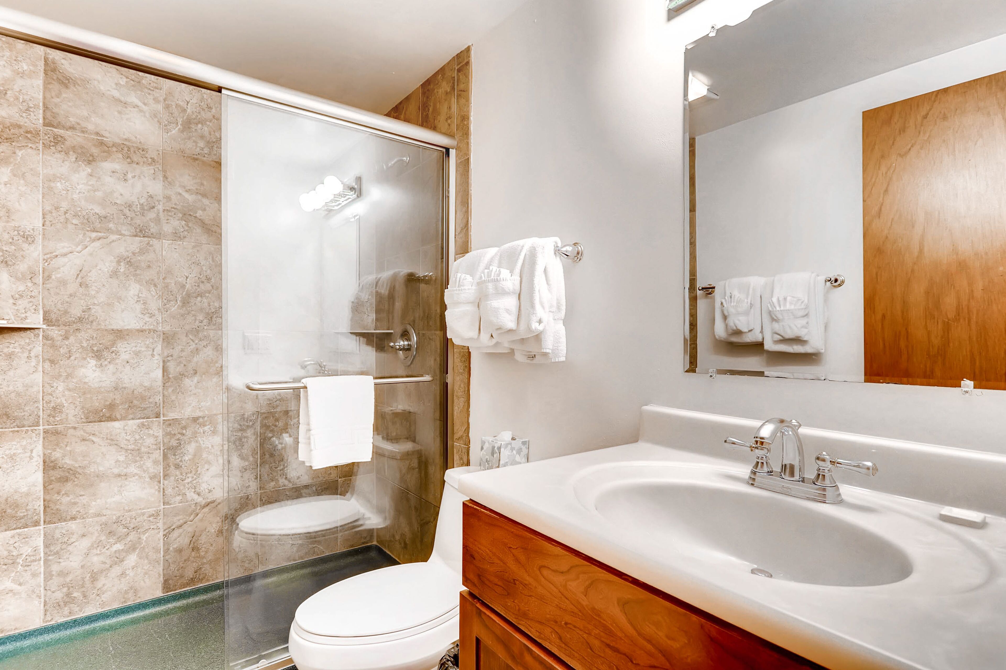 Une salle de bain moderne avec une douche à parois de verre, des toilettes blanches et un grand lavabo avec un meuble-vasque en bois.