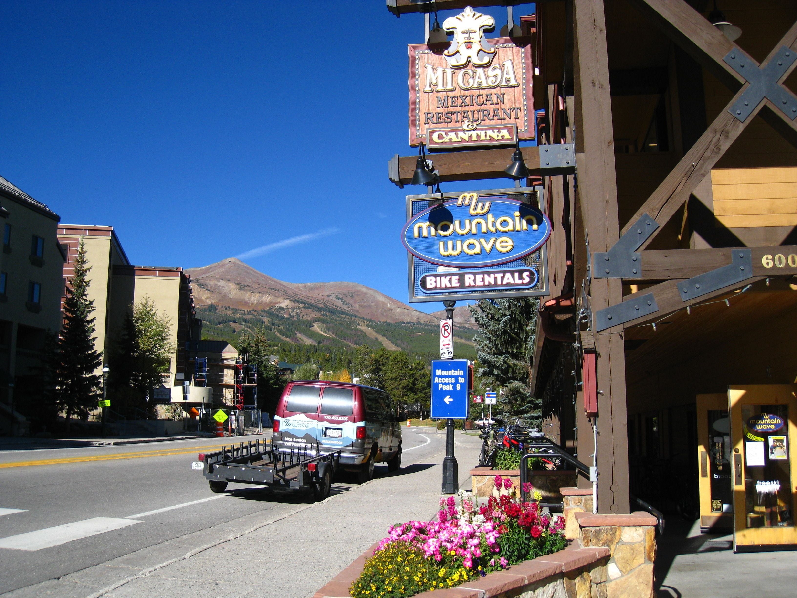 A street view with a sign for 'Mountain Wave Bike Rentals' and a 'Mountain Access to Peak 9' sign.