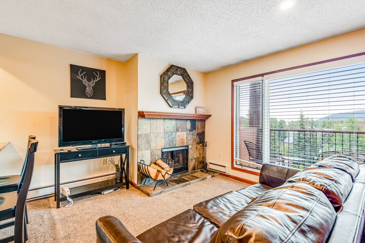 A living room with a fireplace, a television, and a large window with a view of the outdoors.