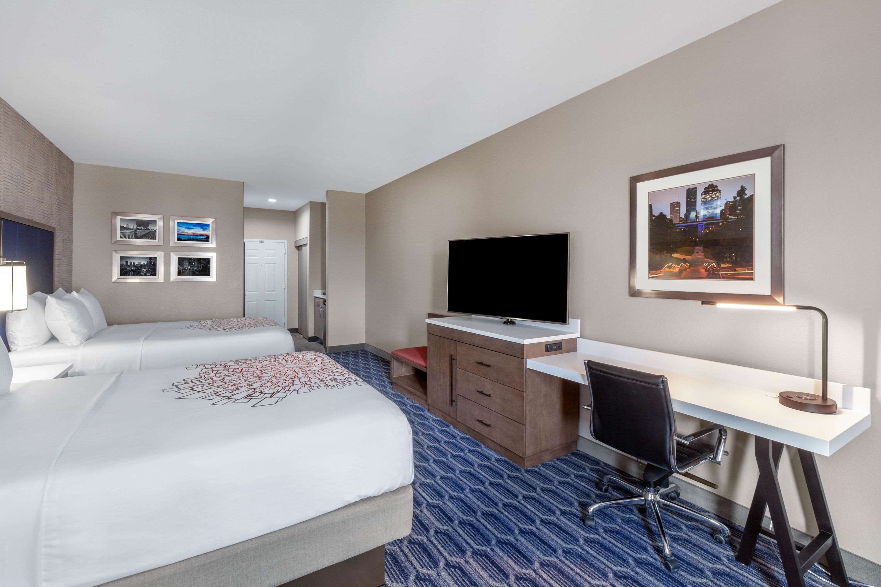 Habitación de hotel con dos camas, un escritorio, una silla, un televisor y cuadros en la pared.