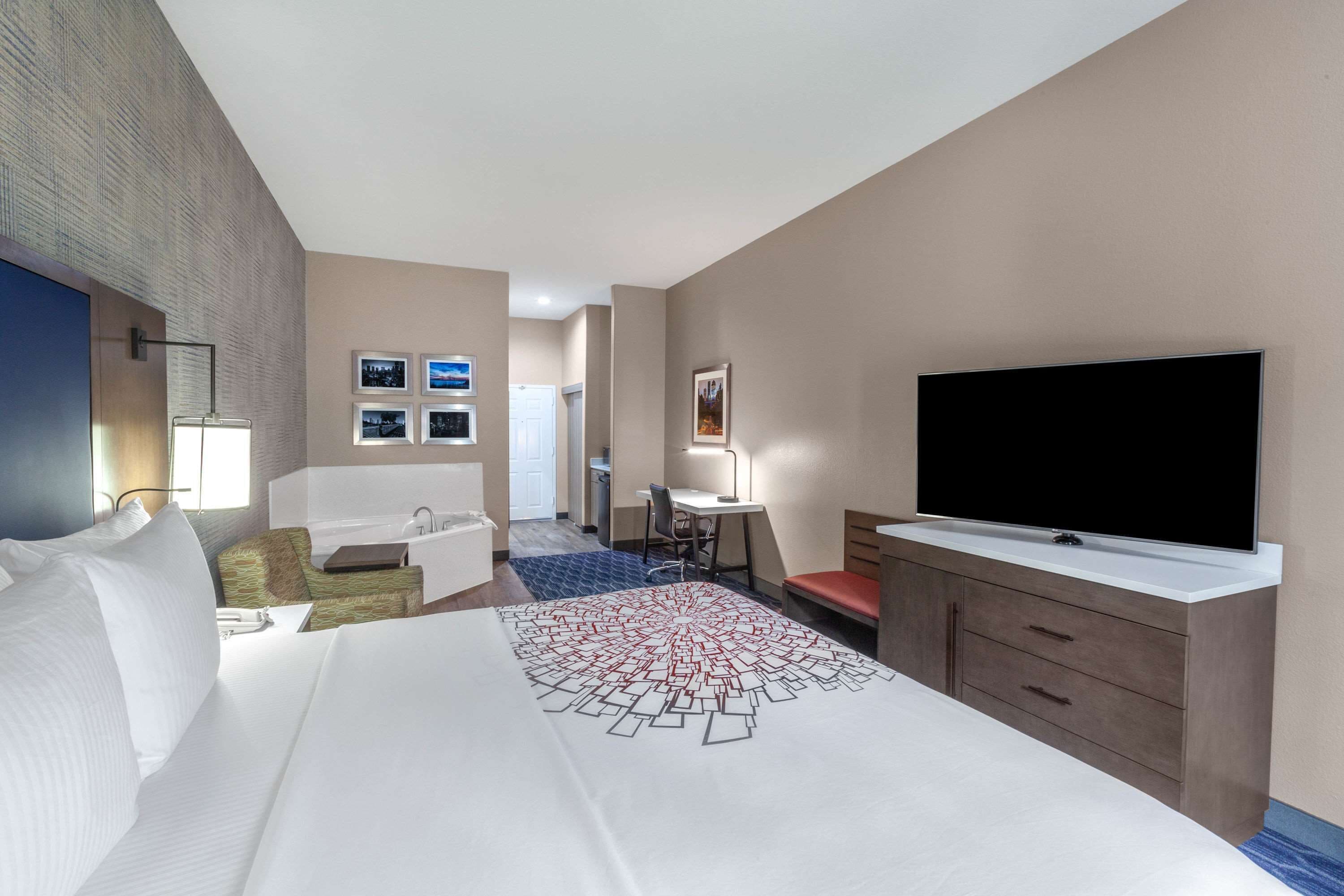 Habitación de hotel con cama, escritorio, silla, televisión y baño.