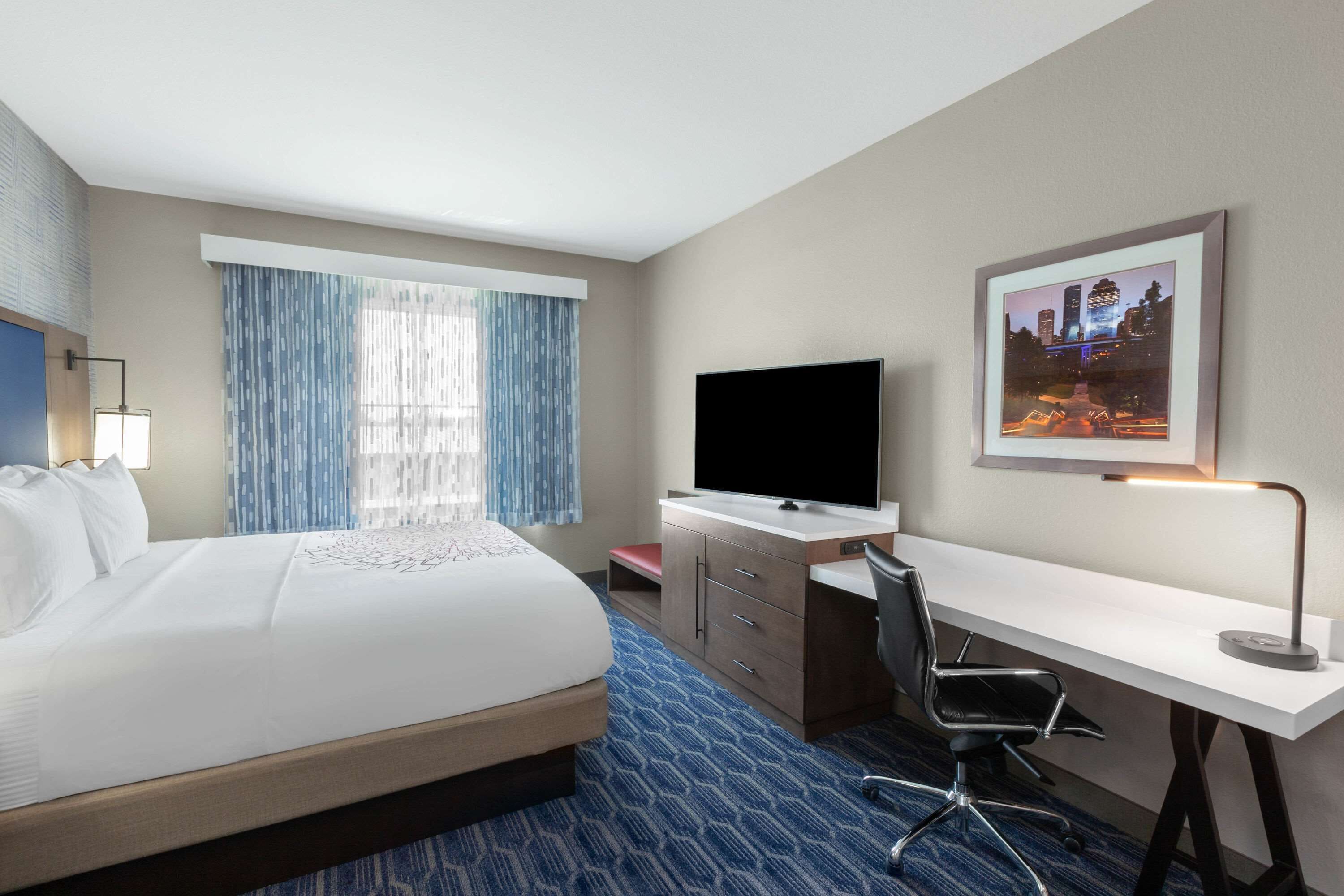 A hotel room with a bed, a desk, a chair, a television, and a window with curtains.