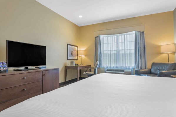 A hotel room with a large bed, a desk with a chair, a television, and a window with curtains.