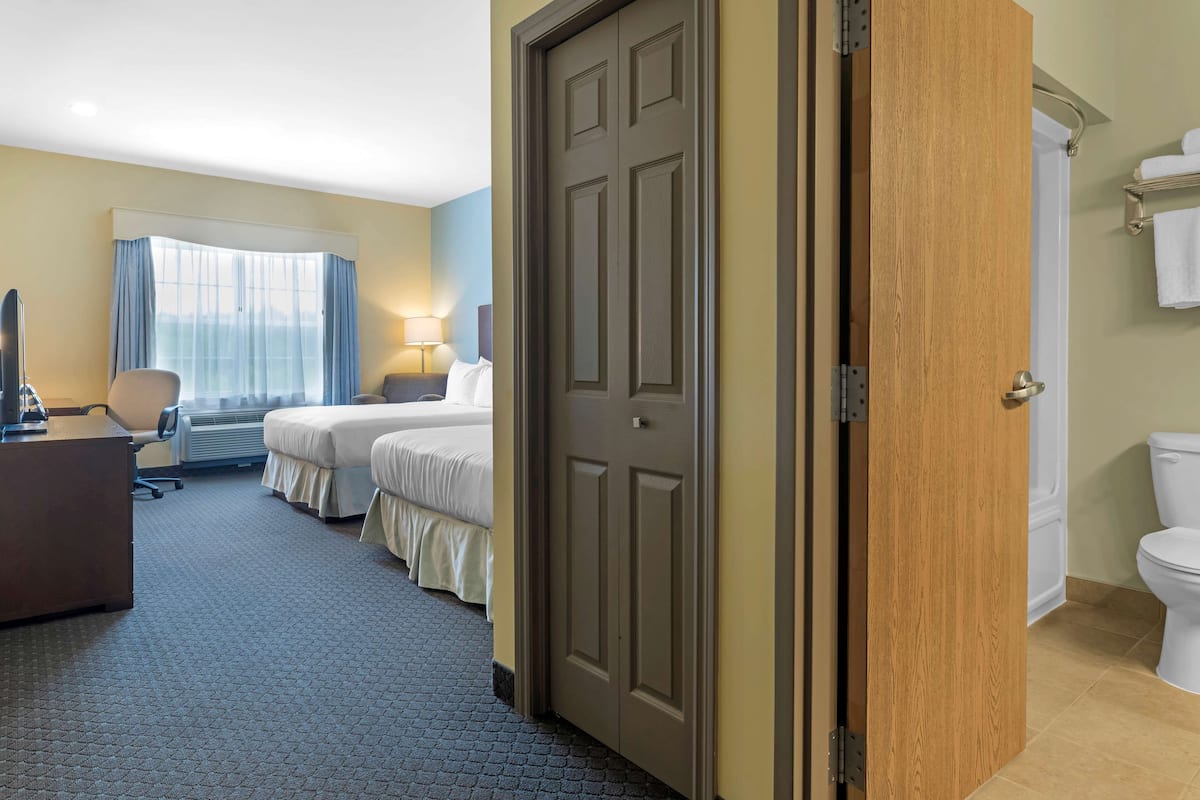 A hotel room with a bed, a desk, a chair, a window with curtains, a door, and a toilet.