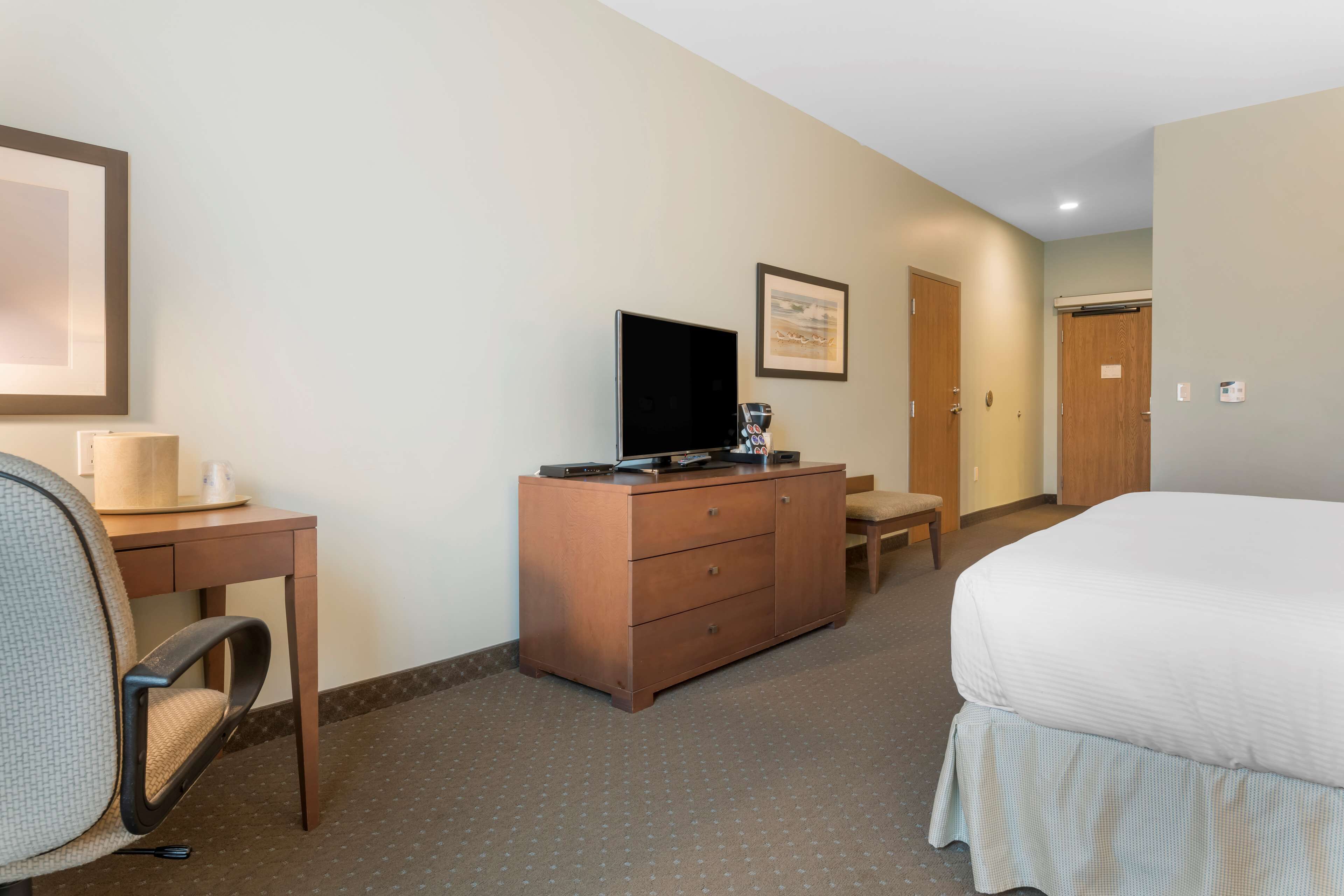 A hotel room with a bed, a desk with a chair, a dresser, a television, and a framed picture on the wall.