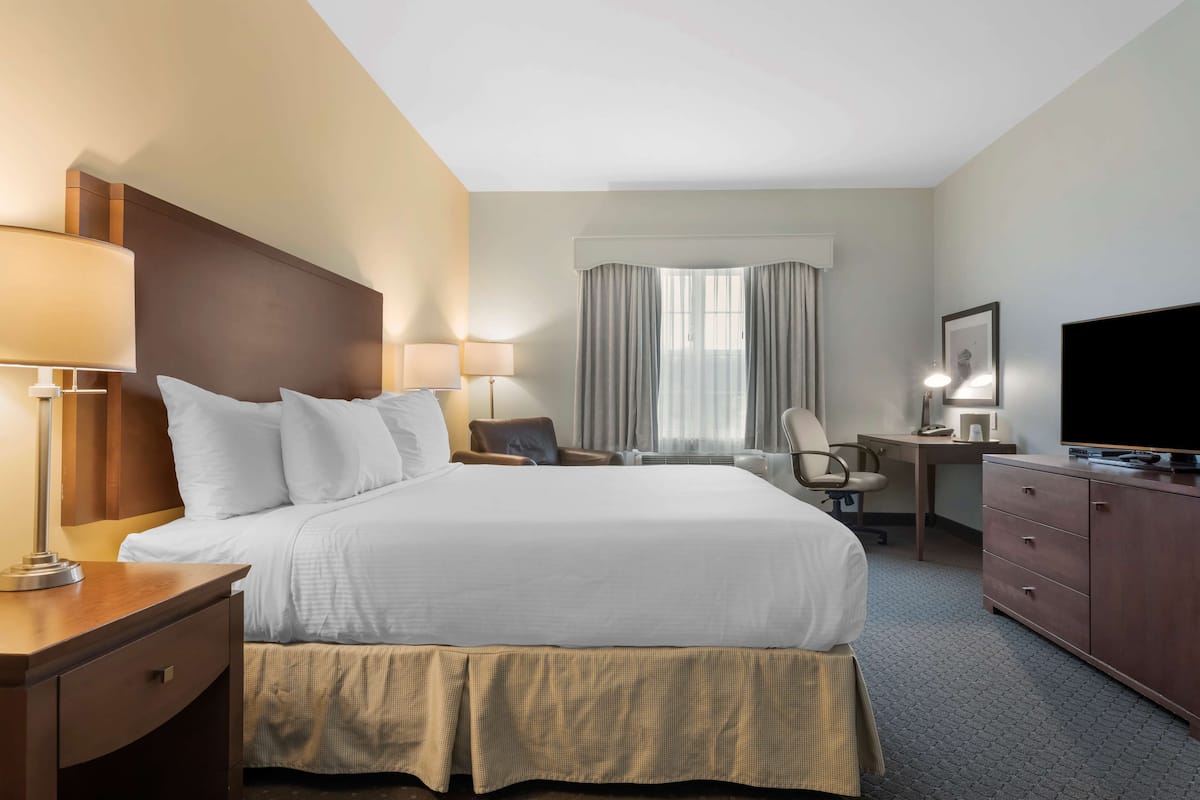 A hotel room with a large bed, bedside tables, a desk, a chair, a television, and a window with curtains.