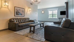 A living room with a brown leather sofa, a wooden coffee table, and a chandelier. - Best Western Plus Liverpool Hotel & Conference Centre (Brooklyn)
