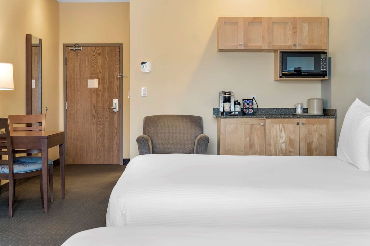 A hotel room with a bed, a chair, a desk with a coffee maker, and a microwave.