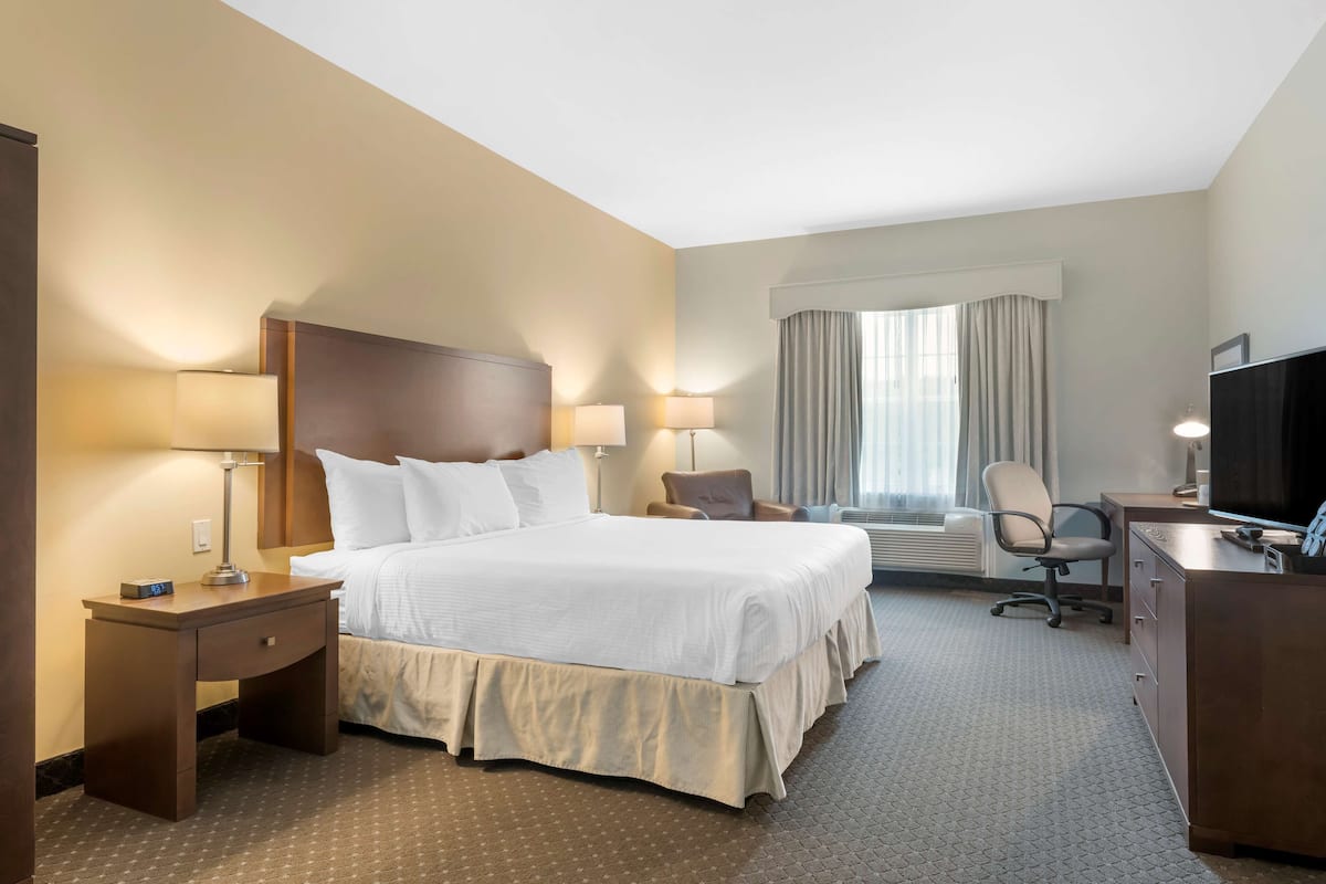 A hotel room with a large bed, bedside tables with lamps, a desk with a chair, a television, and a window with curtains.