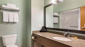 A bathroom with a white toilet, a sink, and a mirror. There are towels on a rack and a black bag on the counter.