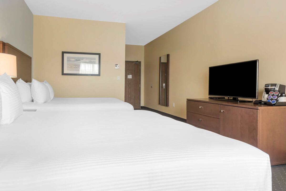 A hotel room with two beds, a television, a coffee maker, and a framed picture on the wall.