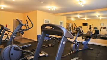 Un gimnasio con equipo de ejercicio, un espejo grande y un reloj en la pared.