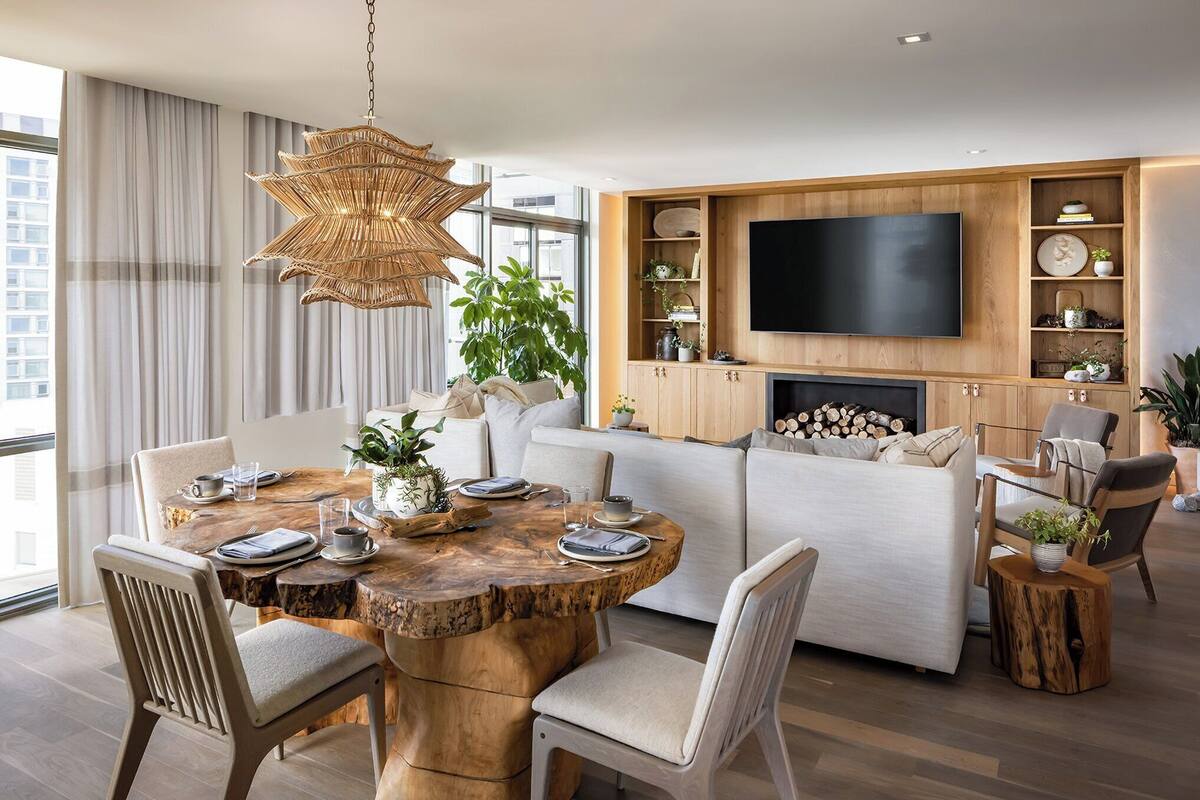 Un salon moderne avec une table à manger ronde en bois, des canapés blancs, un téléviseur à écran plat et des étagères intégrées ornées d’objets décoratifs.