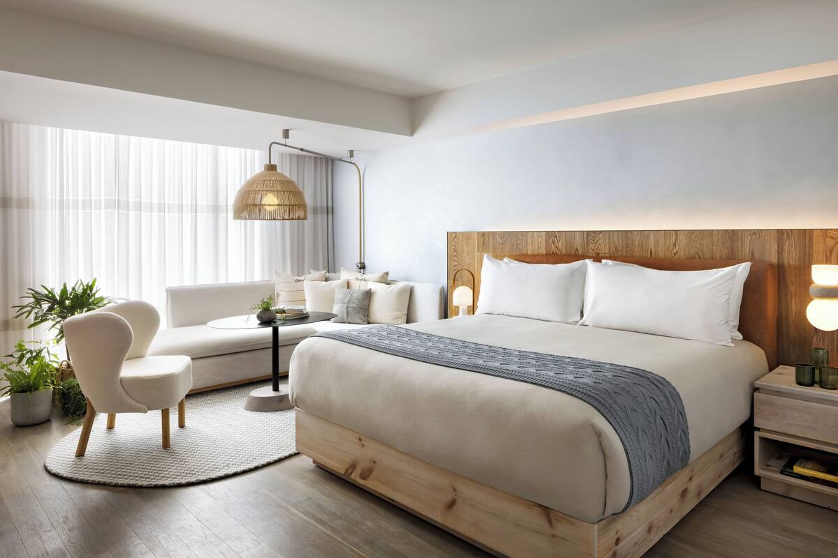 Une chambre d’hôtel moderne, dotée d’un grand lit, d’un canapé, d’un fauteuil et d’une table de chevet avec une lampe.