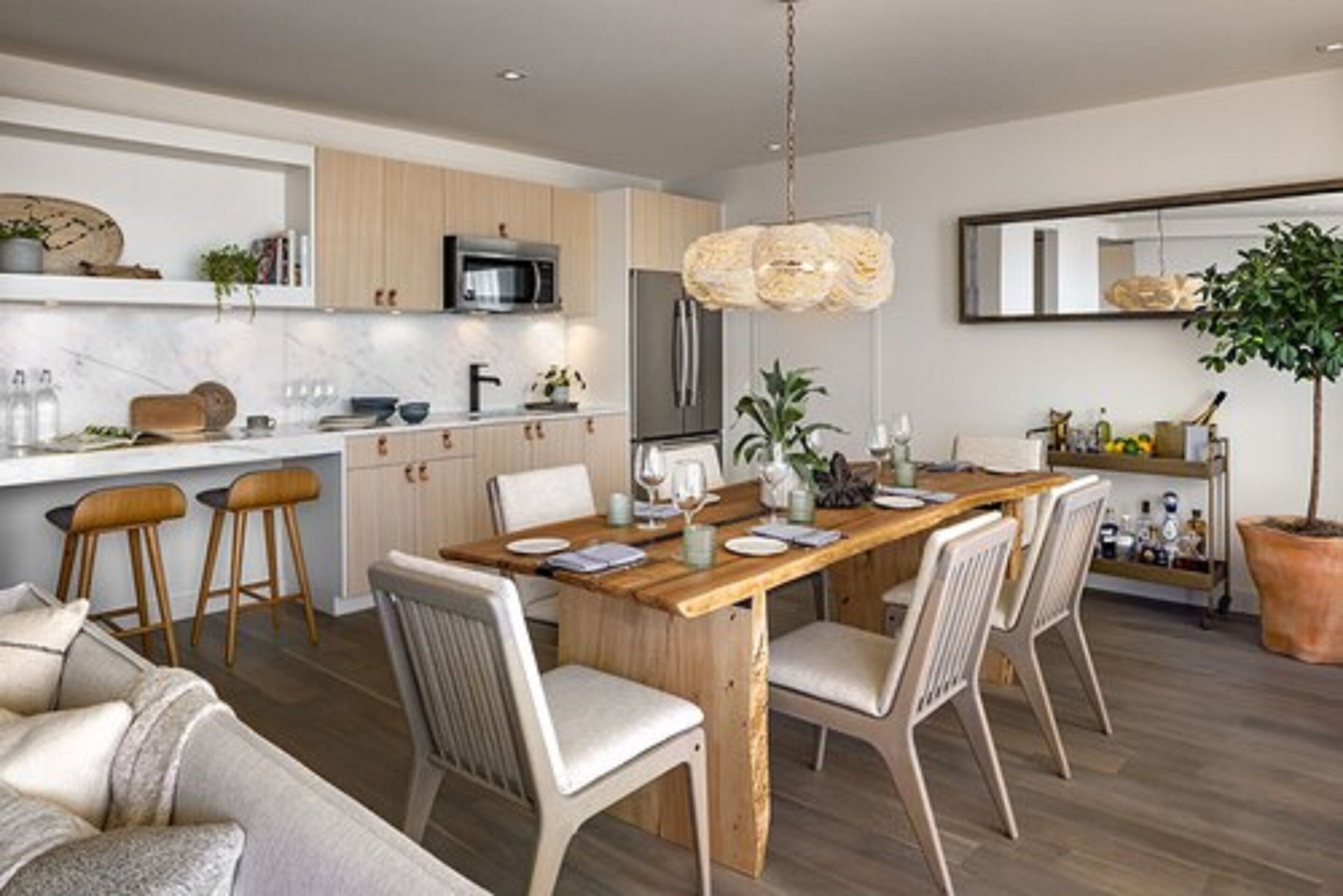 A modern kitchen with a wooden dining table, bar stools, and a hanging light fixture.