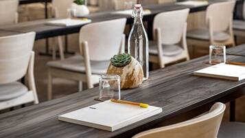 Une salle de conférence avec de longues tables, des chaises blanches, une bouteille en verre, un petit verre et un carnet.