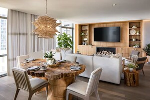 Een moderne woonkamer met een grote televisie, houten kasten en een eethoek met een ronde tafel.