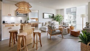 A modern kitchen with wooden stools, a dining area with a white sofa, and a large window providing a view of the city. - 1 Hotel Toronto (Toronto)