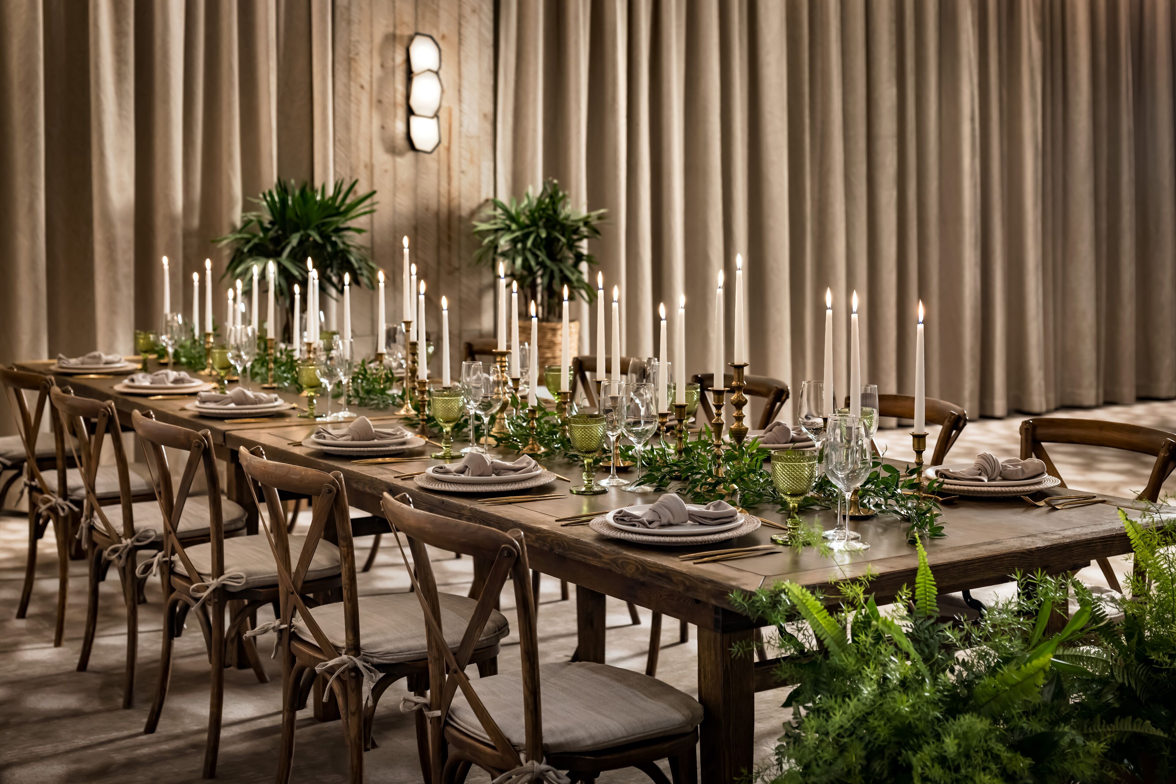 A long dining table set with candles, plates, glasses, and greenery.