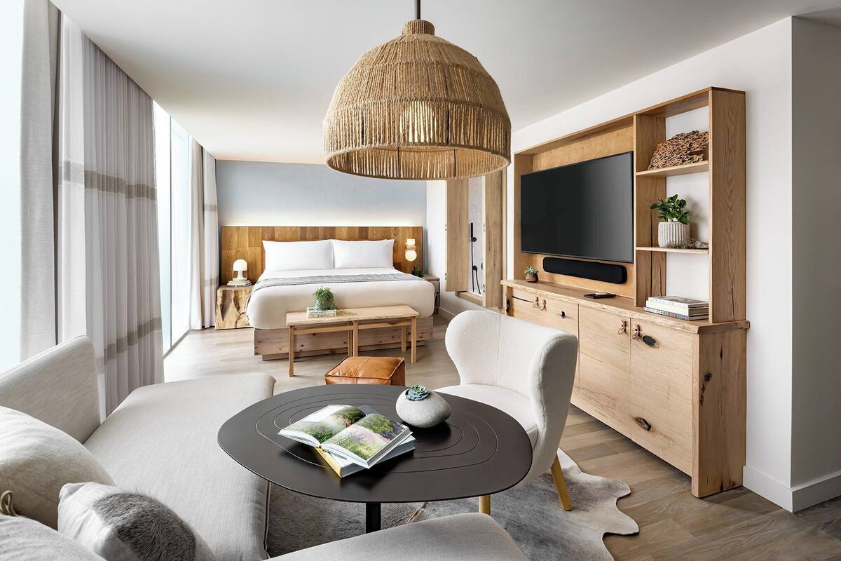 Une chambre d’hôtel moderne avec un grand lit, une télévision, une armoire en bois et une table ronde sur laquelle est posé un magazine.