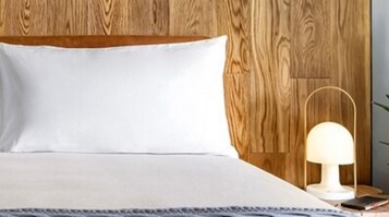 Een net opgemaakt bed met een wit kussen en een houten hoofdbord.