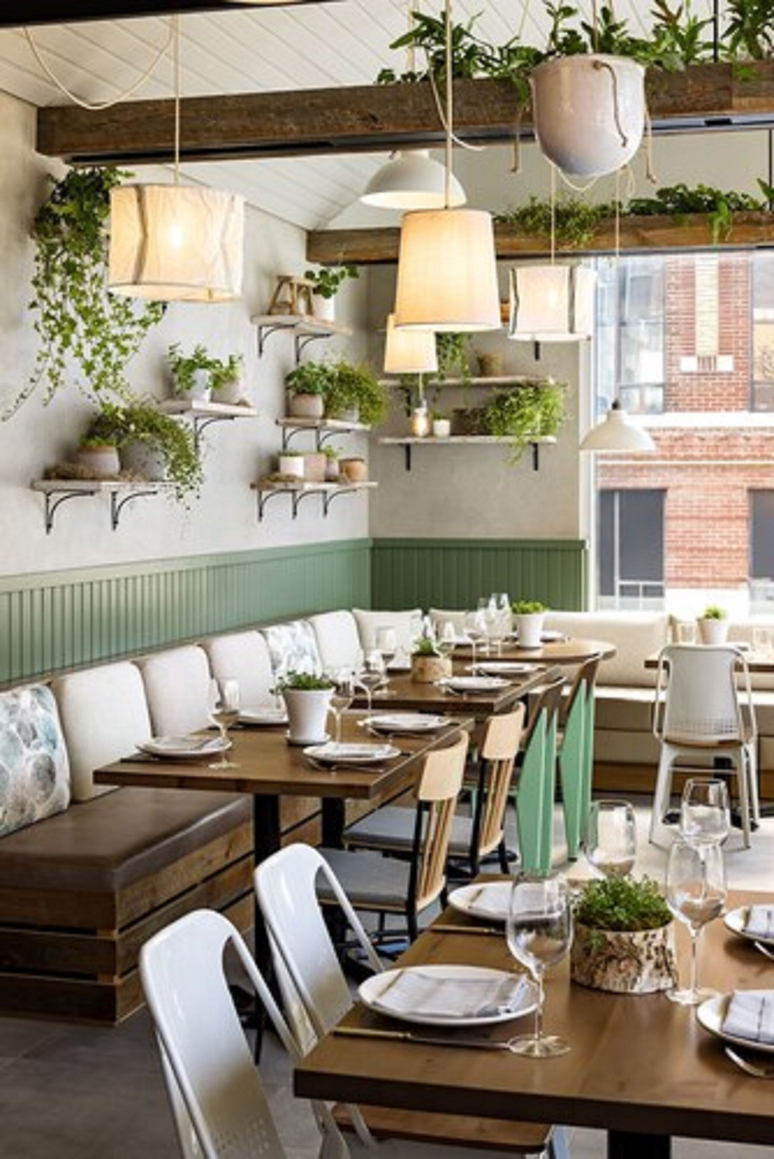 Un restaurant avec des tables et des chaises en bois, des plantes suspendues et des lampes pendantes.