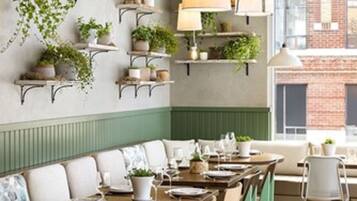 Un restaurant avec des tables et des chaises en bois, des plantes suspendues et des lampes pendantes.