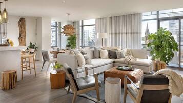 Una sala de estar moderna con un sofá, sillones, una mesa de centro y ventanas amplias con vistas a la ciudad.