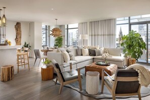 A modern living room with a sofa, chairs, a coffee table, and large windows offering a city view.