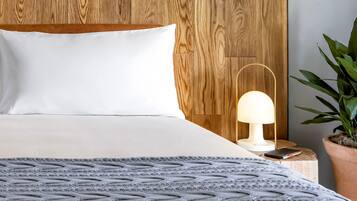 Una cama bien hecha con cabecera de madera, una lámpara de noche y una planta en maceta.