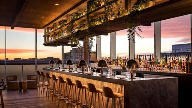 A bar with a long counter, multiple stools, and a view of the cityscape at sunset. - 1 Hotel Toronto (Toronto)