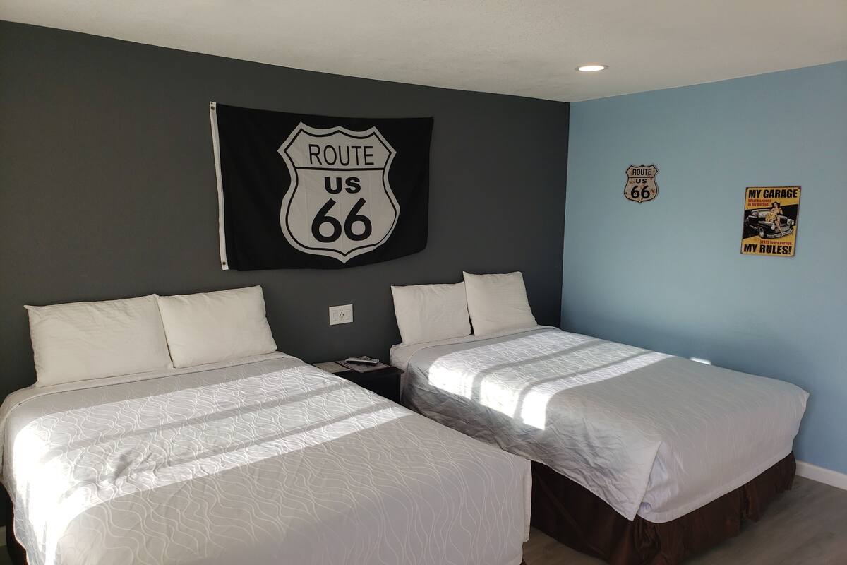 A hotel room with two beds, a Route 66 sign, a Route 66 poster, and a 'My Garage' sign.