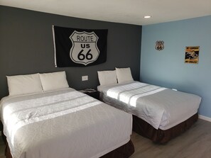Quarto de hotel com duas camas, um letreiro Route 66, um cartaz Route 66 e um letreiro 'My Garage'.