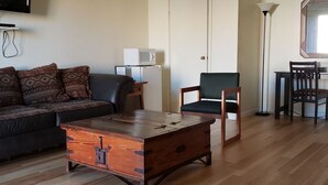 A living room with a wooden coffee table, a sofa, a chair, a television, a microwave, and a door. - Deluxe Inn Motel (Seligman)
