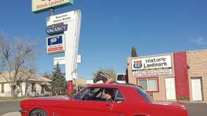 A red vintage car parked in front of a motel with signs indicating a vacancy and amenities like free Wi-Fi and coffee. - Deluxe Inn Motel (Seligman)