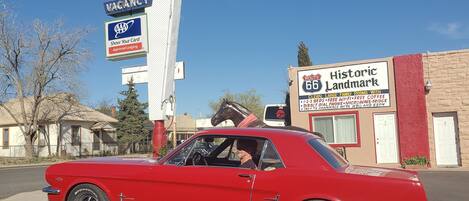 A red vintage car parked in front of a motel with signs indicating a vacancy and amenities like free Wi-Fi and coffee.