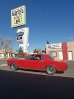 A red vintage car parked in front of a motel with signs indicating a vacancy and amenities like free Wi-Fi and coffee.