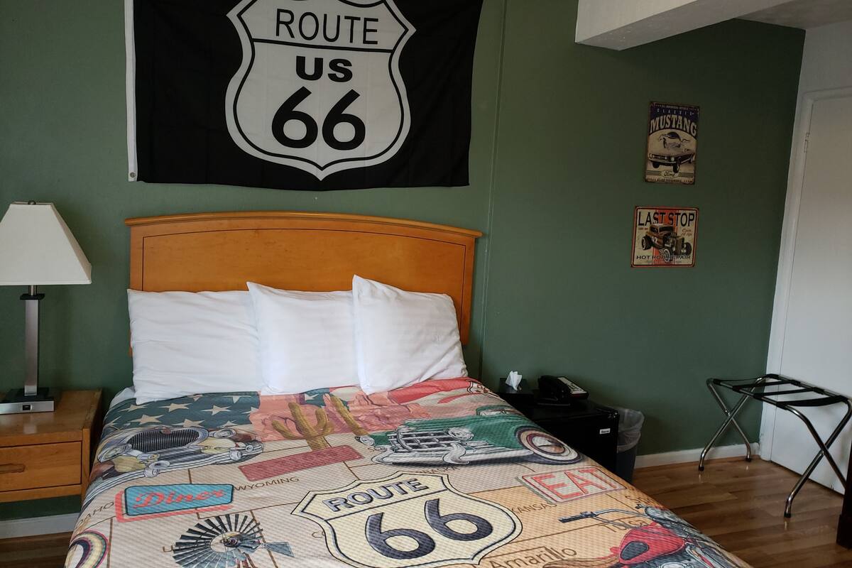 A room with a bed featuring a Route 66 themed bedspread, a Route 66 sign on the wall, and a Mustang poster.