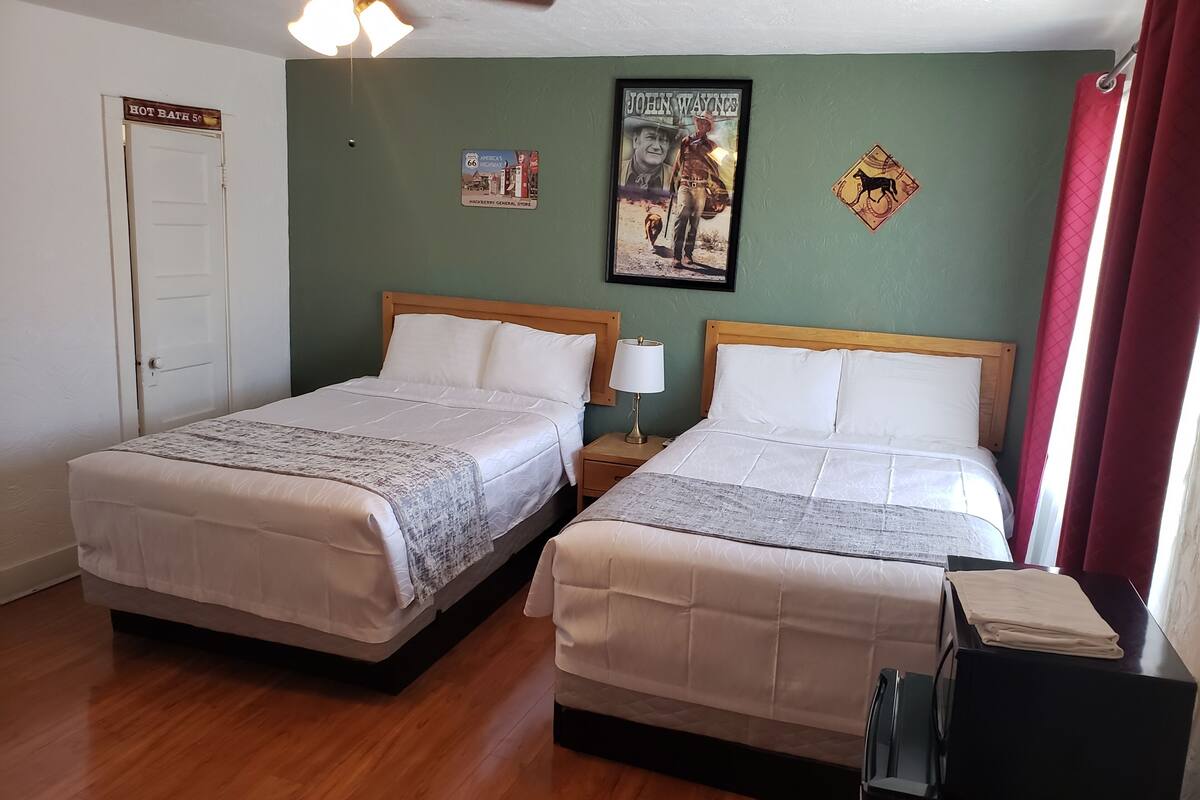 A hotel room with two beds, a ceiling fan, a framed poster, and a door with a sign.
