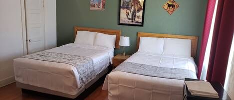 Habitación de hotel con dos camas, un ventilador de techo, un cartel enmarcado y una puerta con un letrero.