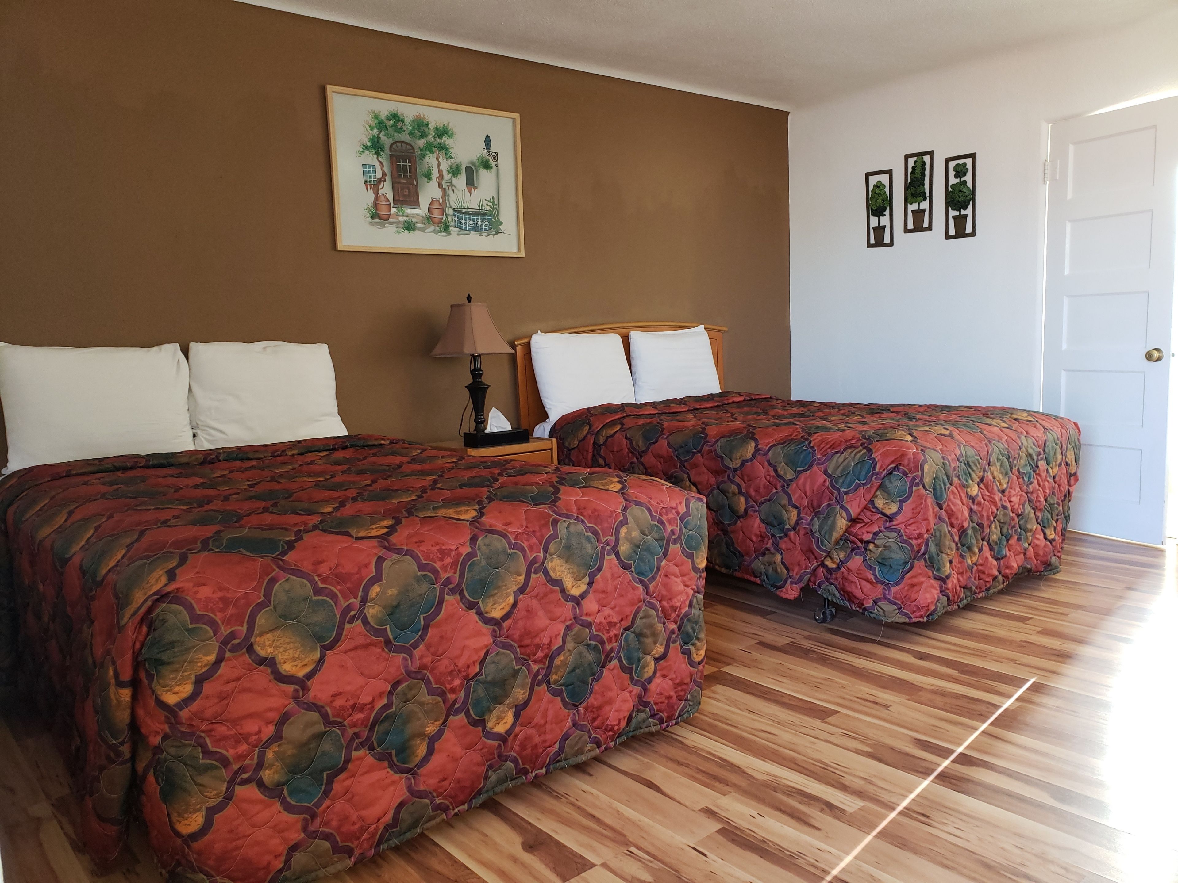 A room with two beds, a wooden floor, a painting on the wall, and a door.