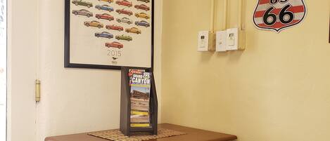 Una habitación con una mesa de madera, un cartel enmarcados de coches, un letrero de Route 66 y un taburete pequeño.