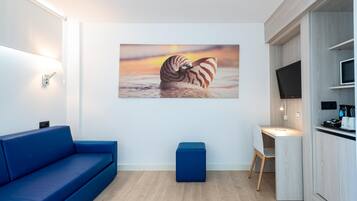 Una habitación moderna con un sofá azul, una mesita, un escritorio, un televisor y una obra de arte en la pared de una criatura marina.