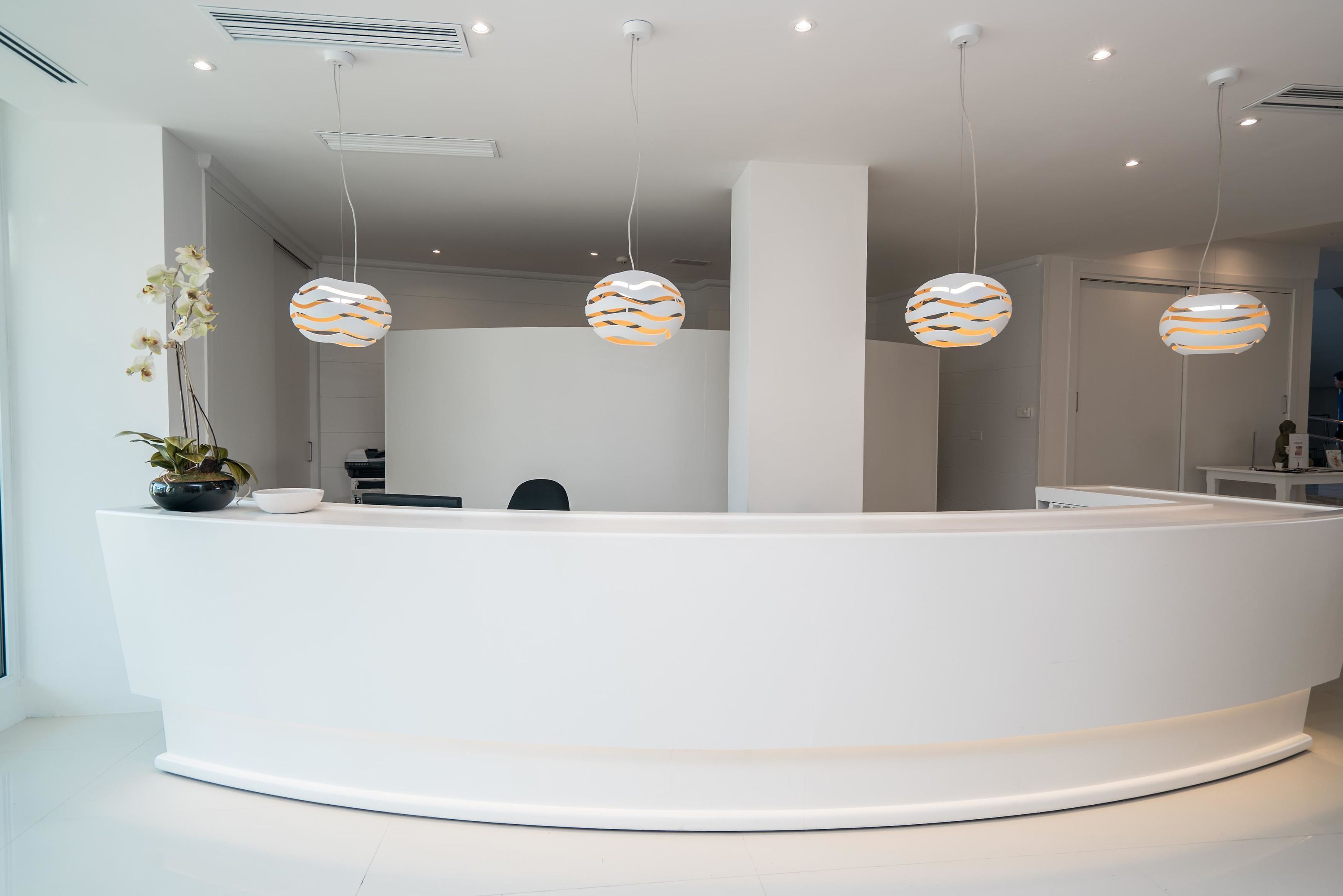 A modern reception desk with three hanging spherical lamps, a potted orchid, and a white reception area.