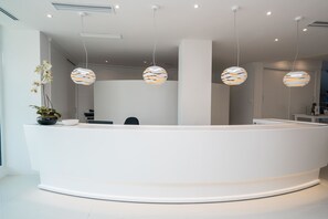 A modern reception desk with three hanging spherical lamps, a potted orchid, and a white reception area. - Hotel THB Sa Coma Platja (Sant Llorenc des Cardassar)