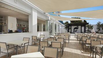 An outdoor café area with tables and chairs, a bar with bottles, and a sheltered seating area with umbrellas.